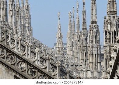 Detailed view of the ornate spires and decorative elements on the rooftop of Milan Cathedral (Duomo di Milano), showcasing Gothic architecture under a bright blue sky - Powered by Shutterstock