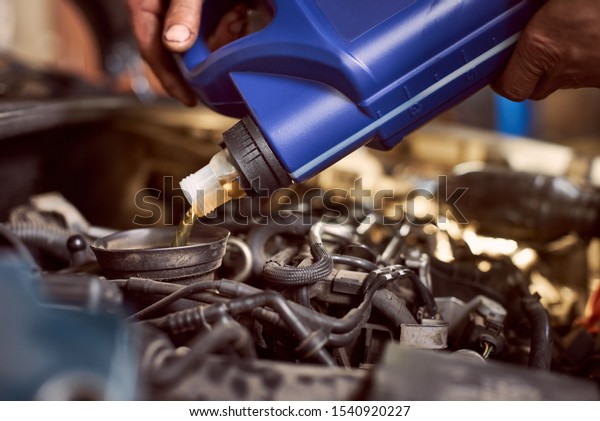 Detailed view of pouring oil into engine.\
Cropped view of blue bottle over auto motor mechanism. Using motor\
oil and engine defender. Maintenance gear and fueling with\
qualitative lubricants