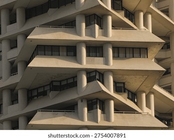 Detailed view of the repeating angular concrete balconies and pillars of a brutalist-style high-rise building under warm afternoon sunlight.