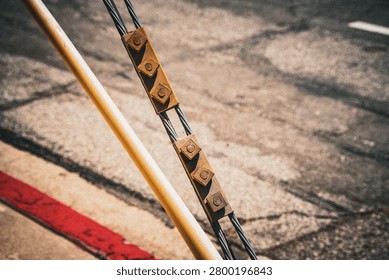 A detailed view of a rusty cable clamp holding multiple wires, positioned next to a smooth yellow pole on a rough, shadowed surface