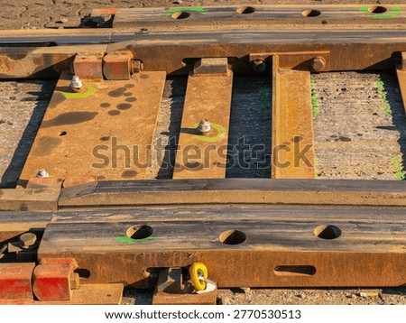 A detailed view of the track elements. The image shows massive steel plates, turnout components, including terminal bolts and rail fasteners, bolted connections with nuts and markings, and rusty rails.