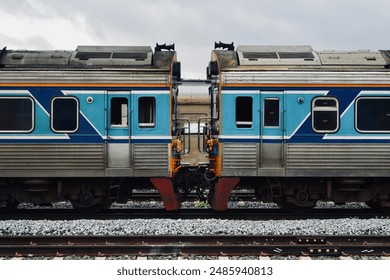 A detailed view of two connected blue and silver train cars on a railway track. The image highlights the mechanical connection and design of modern train transportation. - Powered by Shutterstock