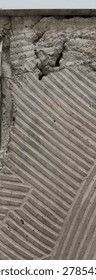 A detailed view of a wall surface, featuring a pattern of diagonal grooves in a greyish-brown material, with a small area of rough, uneven texture and a hint of green, suggesting an unfinished or wea.