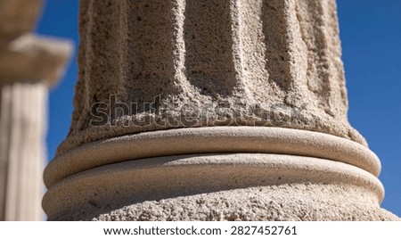 Detailed view of the weathered base of a classical stone column, showcasing its fluted shaft and torus molding against a clear blue sky.