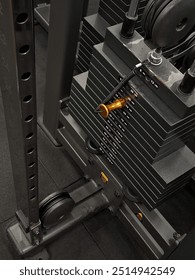 Detailed view of the weight stack on a cable machine in a gym, showing the pin insertion point for weight selection, part of the mechanism, and surrounding structure of the machine.