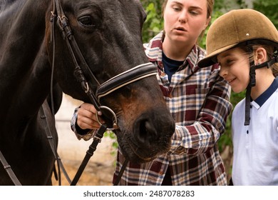 Detailed view of a woman teaching a young rider to adjust a horse's bridle. - Powered by Shutterstock