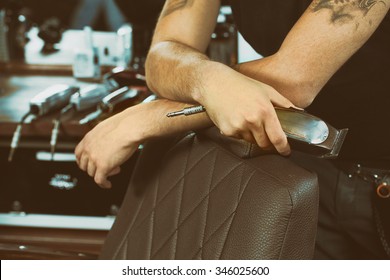 Details in a barbershop. Cropped shot of a barber holding a trimmer in his hand leaning on the leather chair 