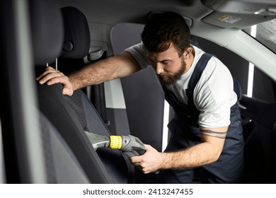 Details of car vacuum cleaning. Professional cropped male worker using wet vacuum cleaner for dirty car interior. Auto car service cleaning the drivers seat, cleaning and vacuuming concept - Powered by Shutterstock