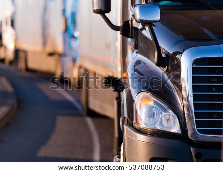 Details of dark semi truck on the road on blured truck and trailer background