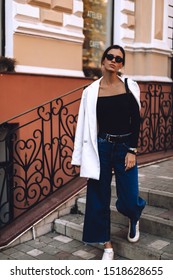 Details Of Everyday Elegant Look. Brunette Model Wearing Casual Outfit. White Blazer, Black Top, Blue Jeans And Sneakers In Trendy Minimalistic Style. Street Fashion For Spring Or Fall Season.