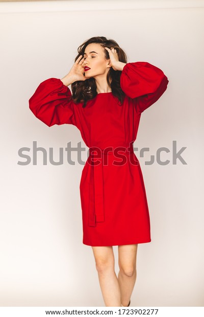 Details of everyday elegant look. Model wearing\
casual outfit. Red color short dress featuring long puff sleeves\
with cuffs in trendy minimalistic style. Lantern sleeves and dress.\
Girl fix hair.