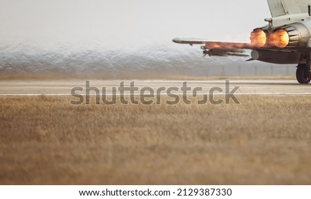 Details with the exhausts of a military jet fighter plane engine while taking off from a tarmac taxiway.
