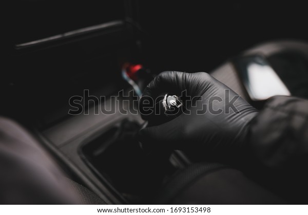 Details with the hand of a driver, in a latex\
glove, on an old and broken gear shift knob of a manual gearbox car\
during the Covid-19\
pandemic.