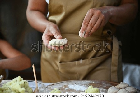 Details: hands of a housewife in chef's apron, sprinkling white flour on a wooden board while hands-on dumplings, cooking homemade varenyky in the country kitchen. Scene of artisanal food preparation