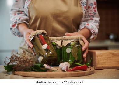 Details: hands of housewife demonstrate to the camera homemade canned food, pickles, pickled chili peppers and marinated cucumbers, on a wooden board with fresh garlic cloves, umbrella dill and herbs - Shutterstock ID 2188293277