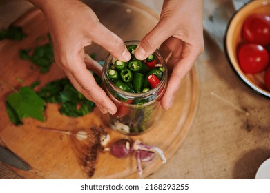 Details: Hands of a housewife, putting ingredients and stacking chili peppers into a sterilized glass jar while canning in the home kitchen. Autumn seasonal canning for the winter. Homemade pickling - Shutterstock ID 2188293255