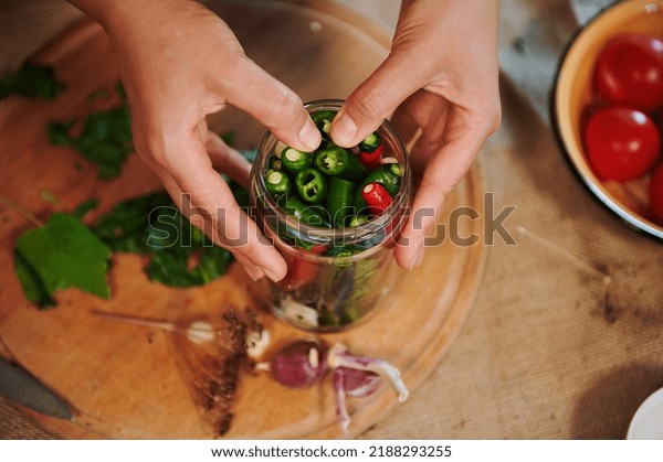 Details: Hands of a housewife, putting\
ingredients and stacking chili peppers into a sterilized glass jar\
while canning in the home kitchen. Autumn seasonal canning for the\
winter. Homemade\
pickling