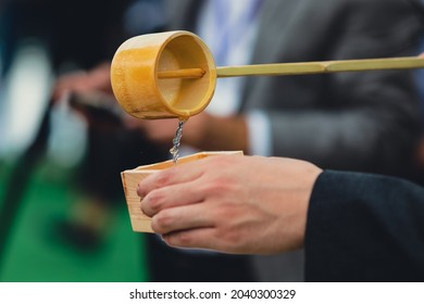 Details With The Hands Of A Man Pouring Traditional Japanese Sake In A Wooden Cup.