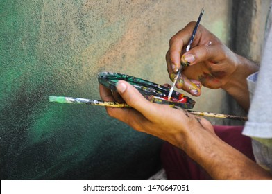 Details Of The Hands Of A Paintor Working With Cans Of Diferents Colors, The Brush On His Fingers  Dirty With Paint While Doing A Mural Art Work Artist Painting