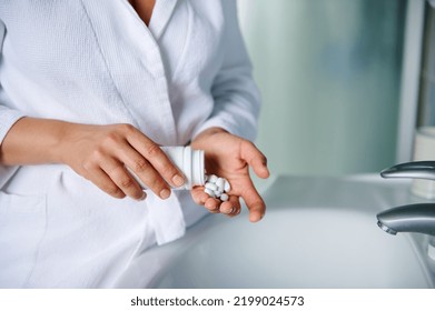 Details: Hands Of A Woman In White Bathrobe, Holding A Container With Pills, Standing At A Sink In Bathroom. Patient Taking Medicine. Compliance To Doctor's Prescription. Healthy Lifestyle. Close-up