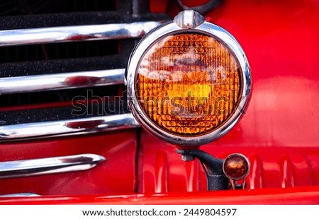 Details of a historic american car. 
Radiator grill with chrome plated element, orange indicator lamp or blinker and colorful red painted body. Oldtimer on Route 66 in Williams, Arizona (USA).