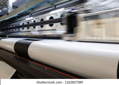 Details from the inside of a large scale professional printer, print head passing by at great speed over vinyl rolls during production hours. 