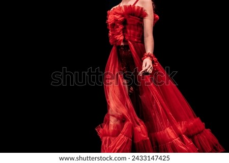 Details of a lush red organza evening dress on a female figure on a black background. Feminine elegant fashion clothes