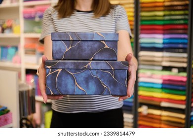 Details on a stack of stylish gift boxes for packing gifts and presents, in the hands of a sales woman working in the creative art shop. People. Hobby. Commerce. Design. Selective focus