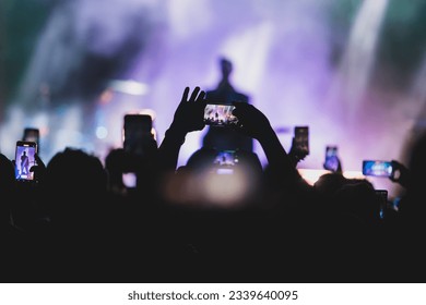 Details of people holding their mobile phone in hand to film a live music concert at night - Powered by Shutterstock