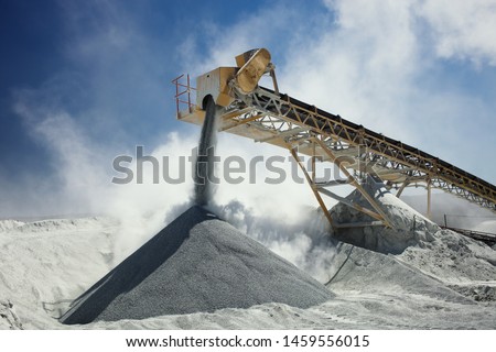 Details of stone crushing equipment at the mining factory in a cloud of dust against the blue sky, close-up. Quarry mining machinery.