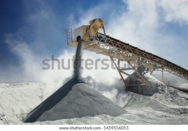 Details of stone crushing equipment at the\
mining factory in a cloud of dust against the blue sky, close-up.\
Quarry mining\
machinery.