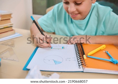 Details: Student's hand holds a pencil and paints the perimeter of a rectangle drawn in a notebook, calculates the perimeter and surface of geometric shapes, doing homework on the geometry at home