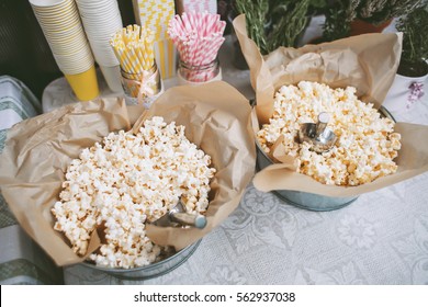 Details of a tasty candy bar with buckets of popcorn and pasteboard pink and yellow glasses