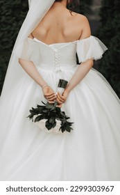 Details of the wedding photo. photo of a bouquet of roses and greenery, which is beautifully held behind her by the bride in a white dress and voluminous veil. Open shoulders.