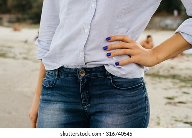 Details of women's clothing. The woman in jeans and shirt standing on the beach. Close-up, outdoors.