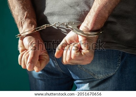 Detained man with hands behind his back. Cutaway view of a handcuffed man in jeans standing, human rights concept.