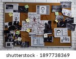 Detective board with fingerprints, photos, map and clues connected by red string on white brick wall