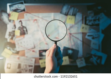Detective hand holding a magnifying glass in front of a board with evidence, crime scene photos and map. high contrast image