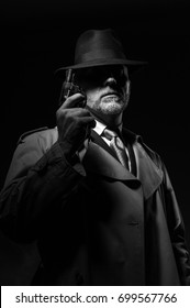 Detective Holding A Gun In The Dark, He Is Wearing A Fedora Hat And A Trench Coat, 1950s Noir Movie Character