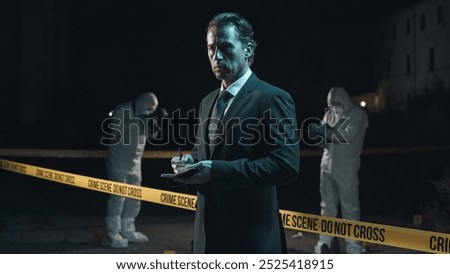 Detective inspecting area and taking notes in notebook at crime scene at night as forensic experts collect evidence behind police tape next to headless body