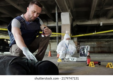 Inspector de detectives en chaleco antibalas sosteniendo una linterna sobre un cadáver mientras inspeccionaba la escena del crimen con un experto criminológico