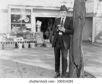 Detective leaning against tree taking notes