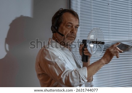 Detective on assignment. A man in a headset stands at a window with blinds, conducting covert surveillance