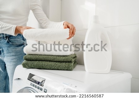detergent gel in white bottle with mockup on automatic washing machine and female with fresh terry towels after laundry in bathroom, cropped shot