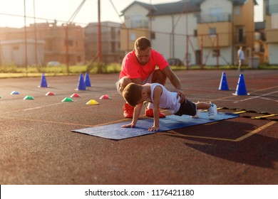 Determinative young football coach learning little boy how to do push ups. Early summer morning training. - Powered by Shutterstock