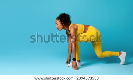 Determined African American Athlete Woman Doing Crouch Start Ready For Running Race, Looking Aside At Copy Space, Over Blue Background In Studio, Wearing Yellow Fitwear. Panorama, Side View Shot