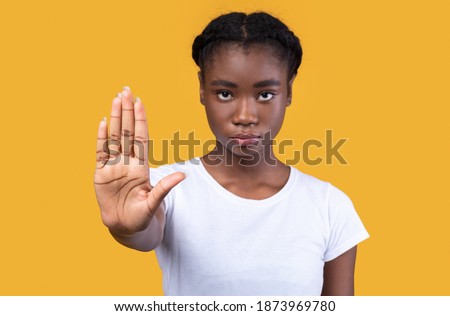 Determined African Woman Gesturing Stop Looking At Camera Warning And Forbidding Something Posing Standing Over Yellow Studio Background. Lady Protesting Against Bullying And Abuse. Selective Focus