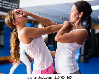 Determined Asian woman practicing basic self-defense techniques in sparring during training in gym, blocking hand of female opponent and launching palm blow in face