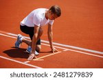 A determined athlete is in a crouched position at the starting line of a red track, prepared to start a sprint race