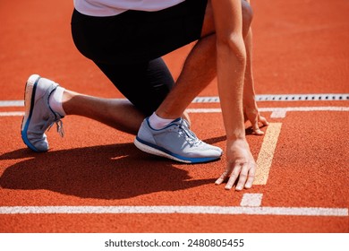 A determined athlete is in a crouched position at the starting line of a red track, prepared to start a sprint race - Powered by Shutterstock